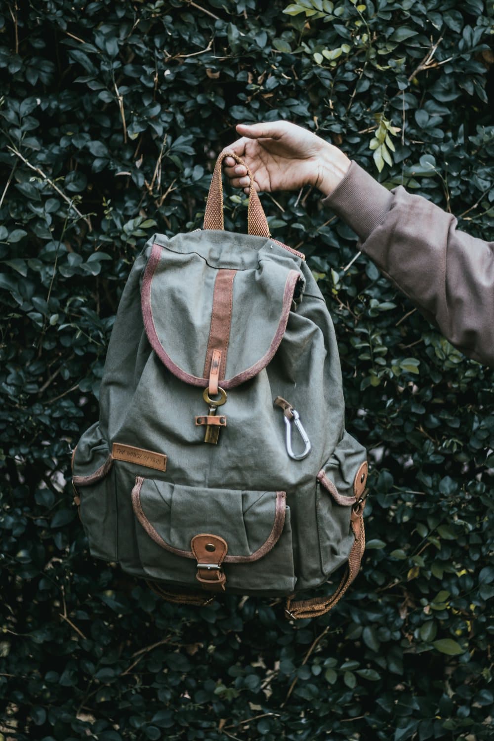 A hand holding a grey canvas rucksack against green leaves