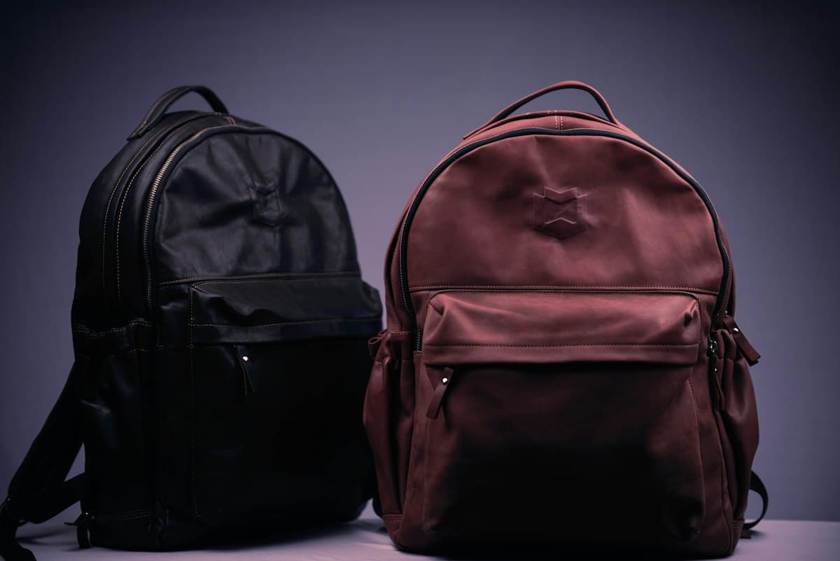 Two leather backpacks, one black and one oxblood, on a studio plinth