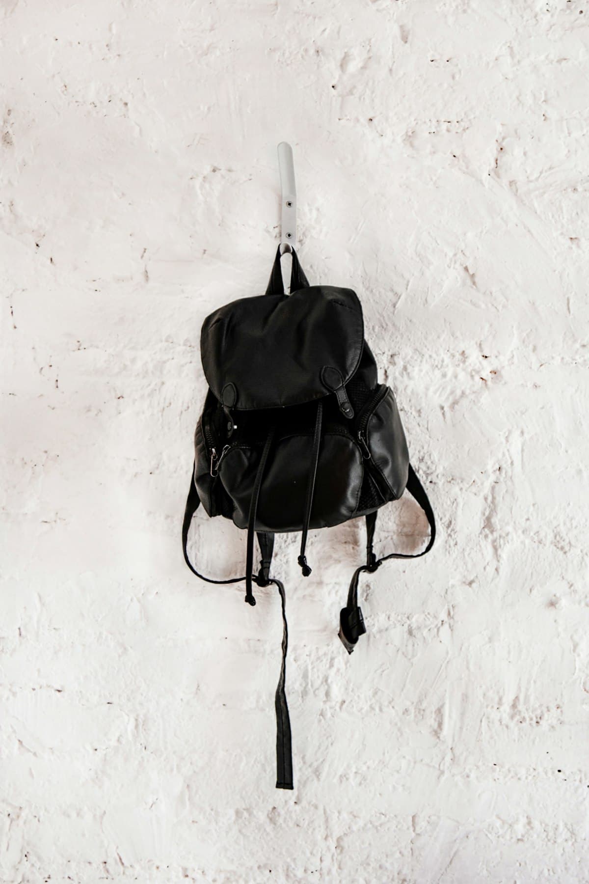 A small black backpack hanging on a white wall