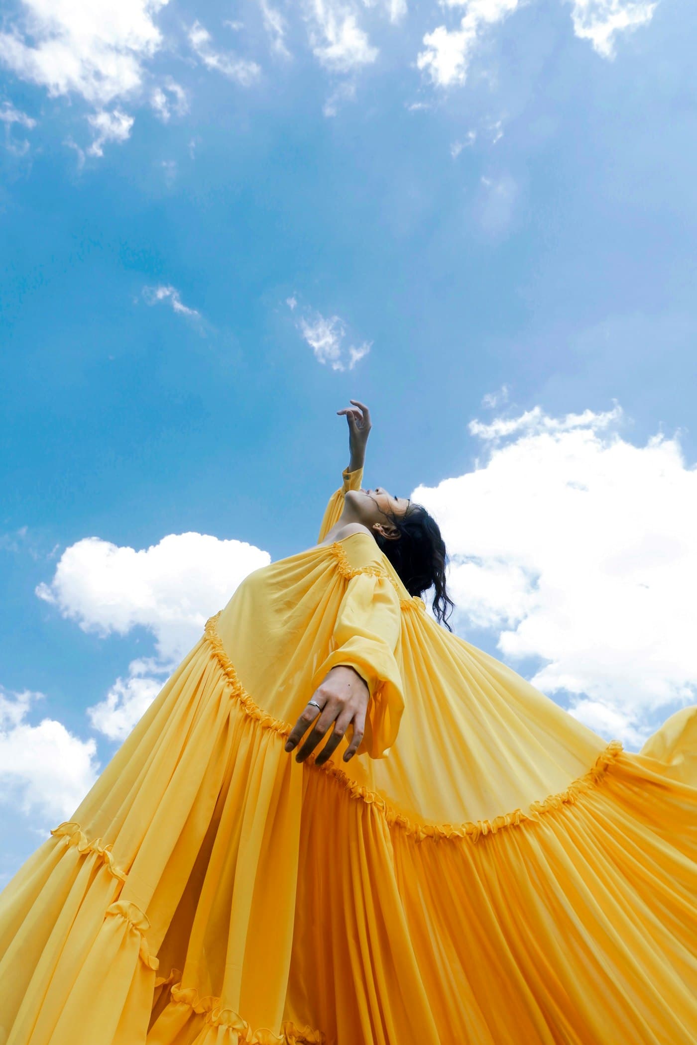 Woman in a flowing yellow pleated dress against a blue sky