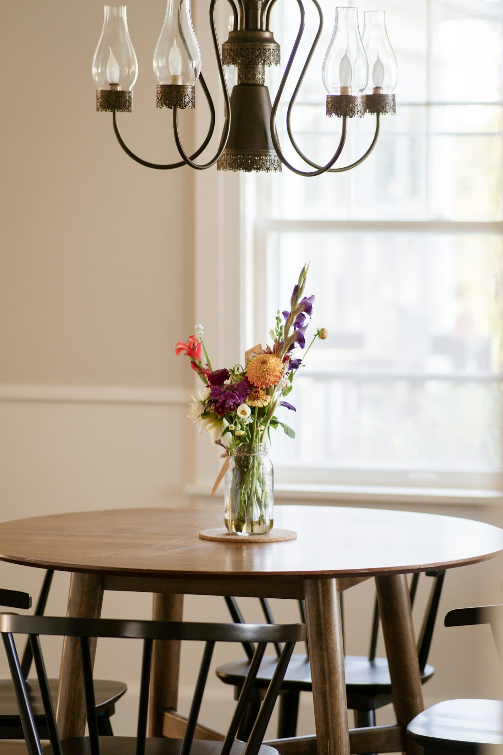 Round dining table with a vase of wildflowers by a window