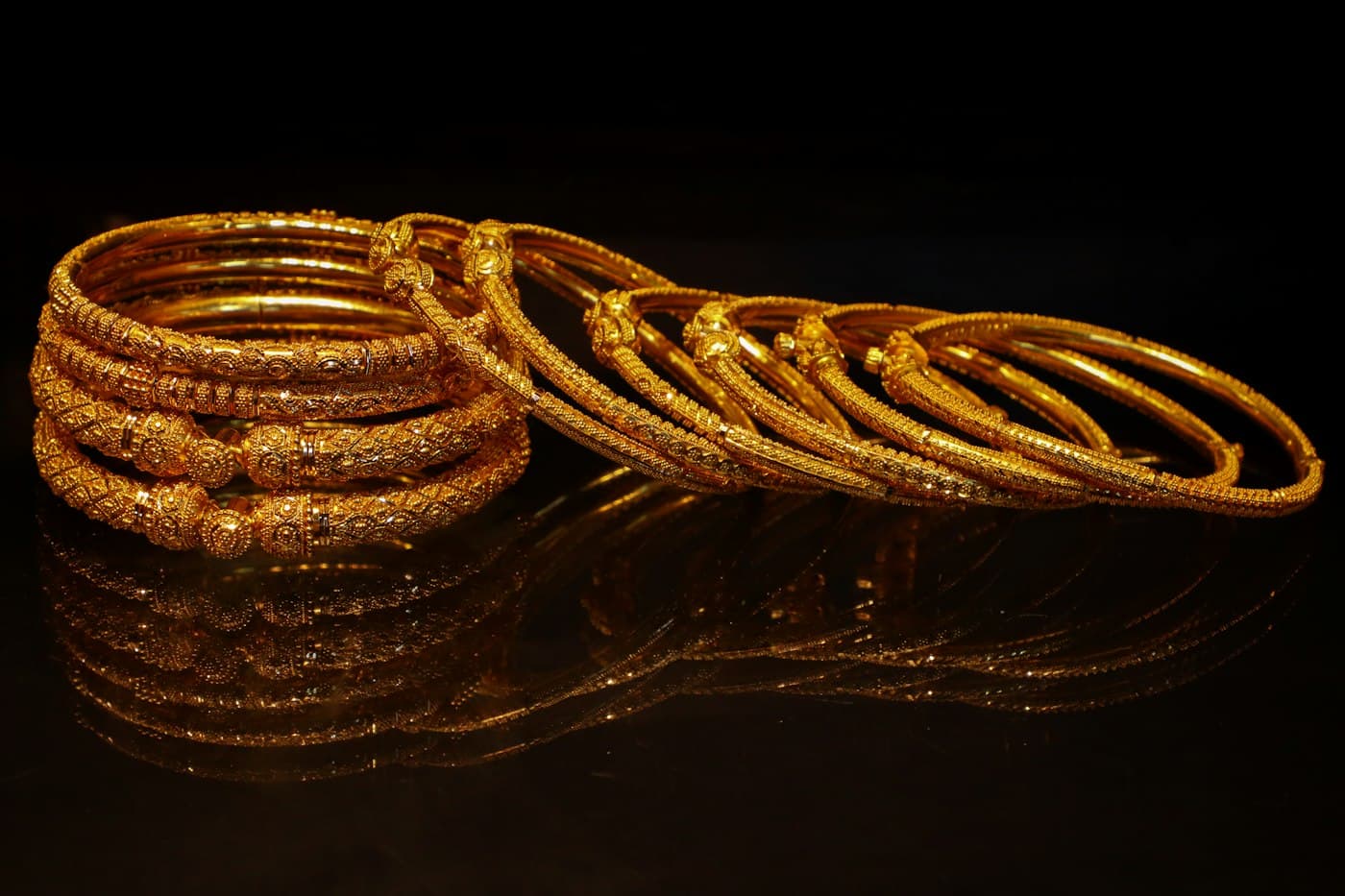 A stack of ornate gold bangles resting on a dark reflective surface