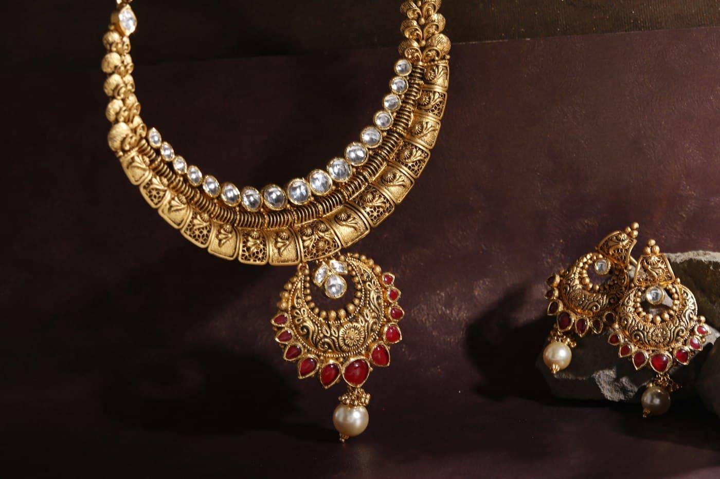 A kundan-style gold necklace with white stones and a ruby drop