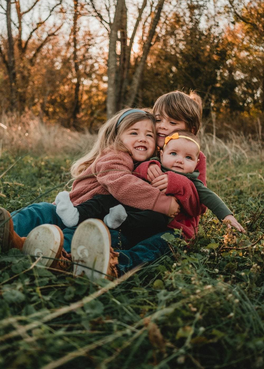 Three smiling children hugging each other on a grassy hillside