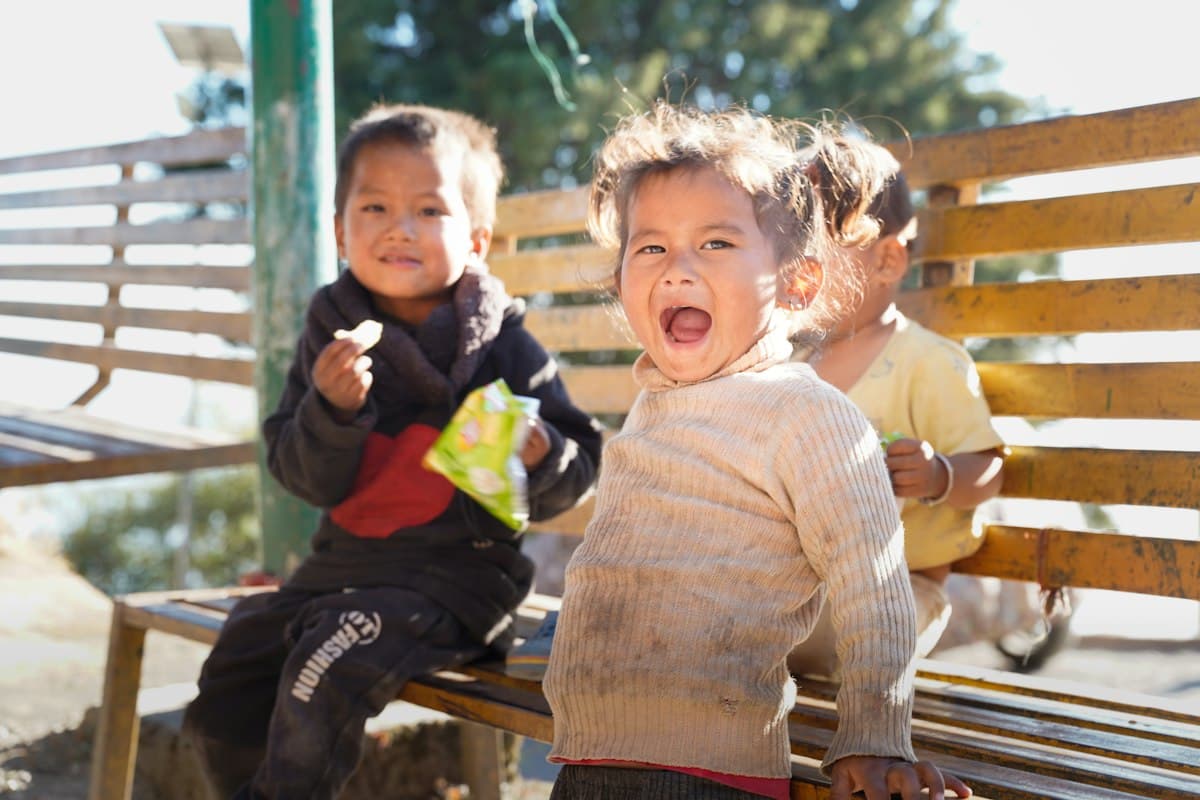 Three children laughing together on a wooden bench