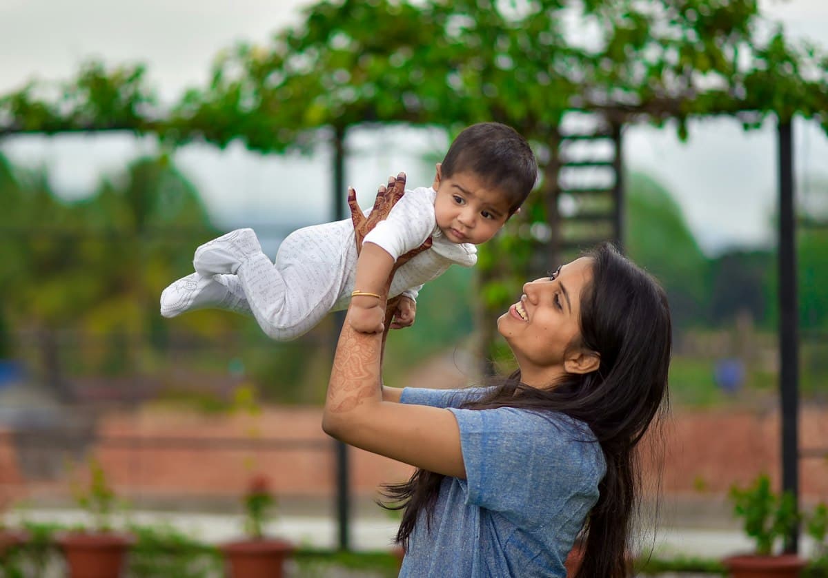 A mother lifting her smiling baby in a garden