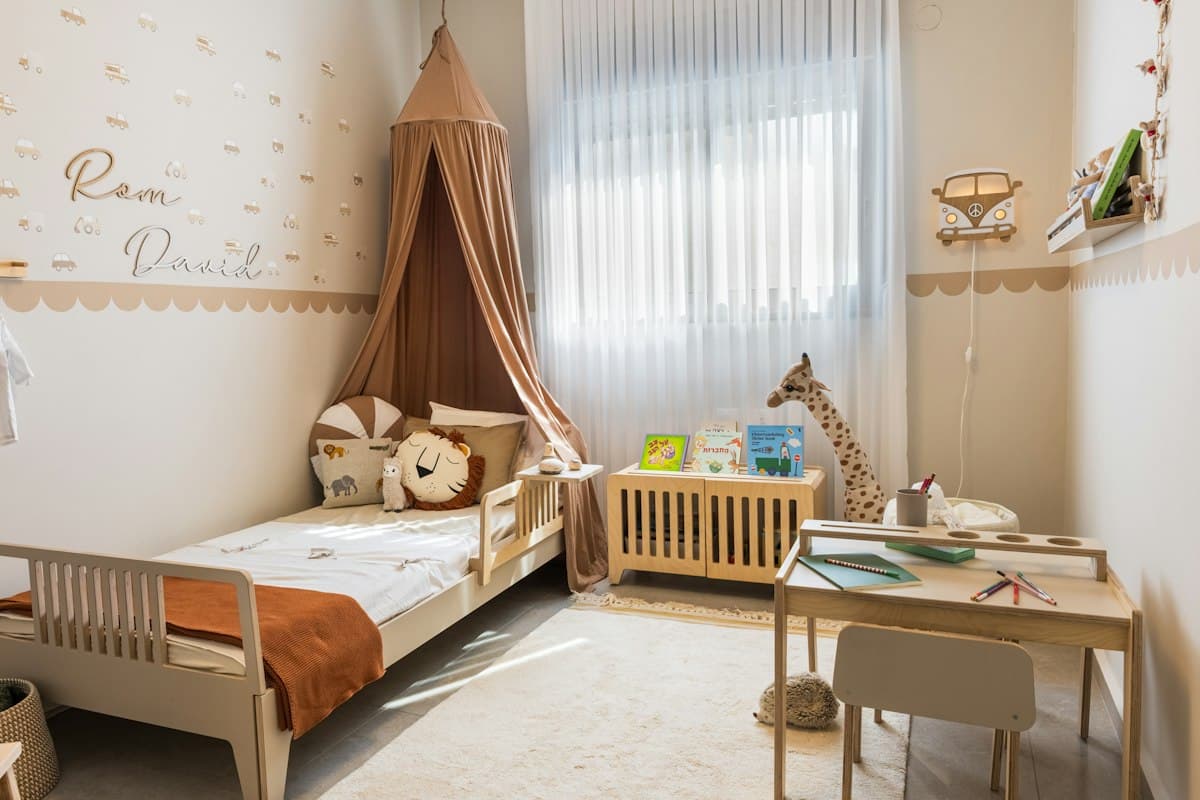 A calm nursery with a canopy, a toddler bed and a wooden desk