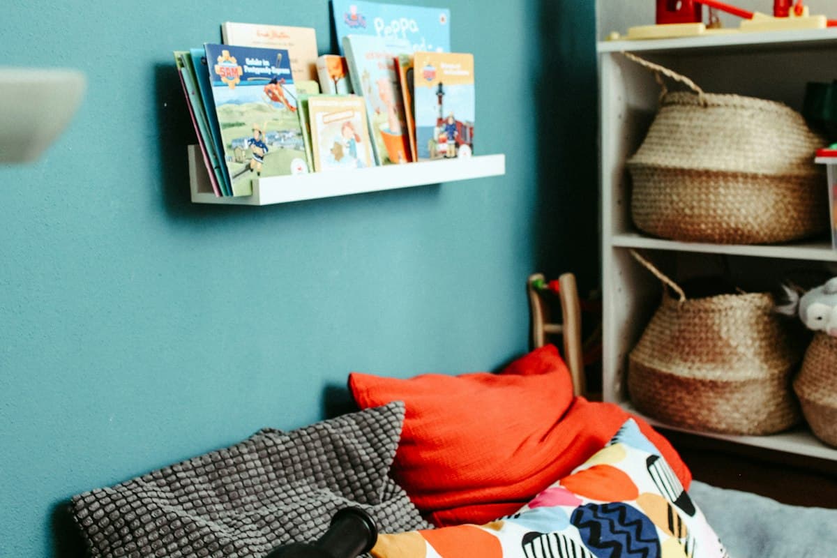 A reading nook with a wall shelf of picture books and a red cushion