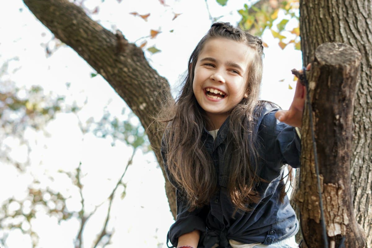 A girl laughing while holding a tree trunk