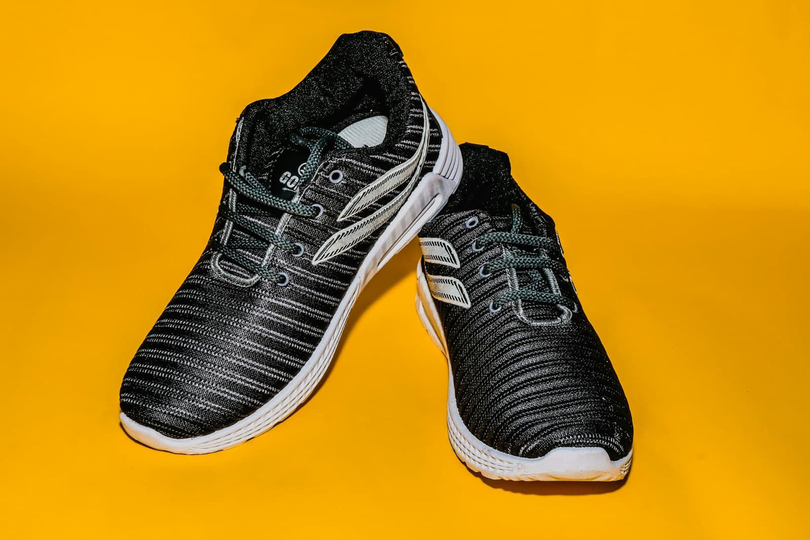Black knit running shoes on a yellow background