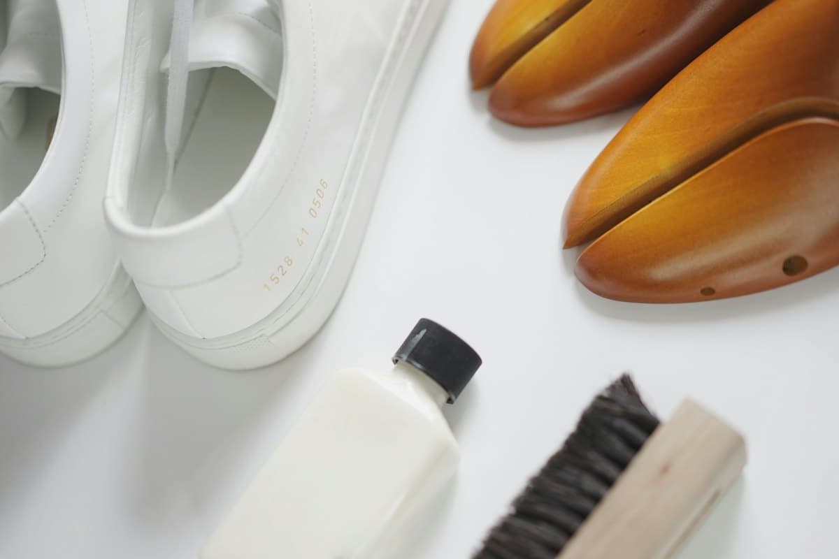 White sneakers beside wooden shoe trees, a brush and cleaning lotion