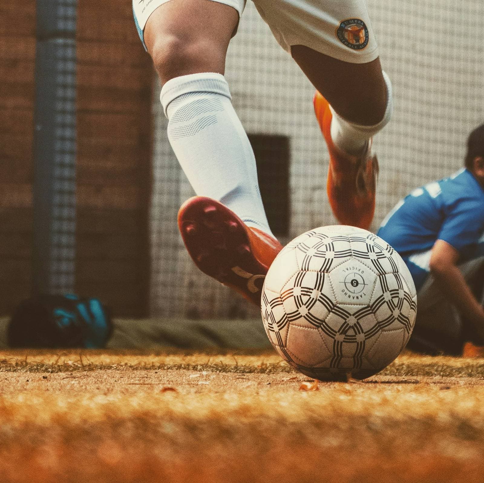A player striking a football on a dusty pitch