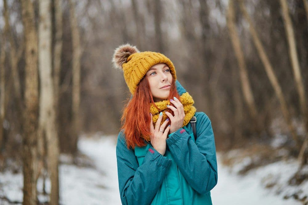 Woman in a teal jacket and mustard beanie in a winter wood