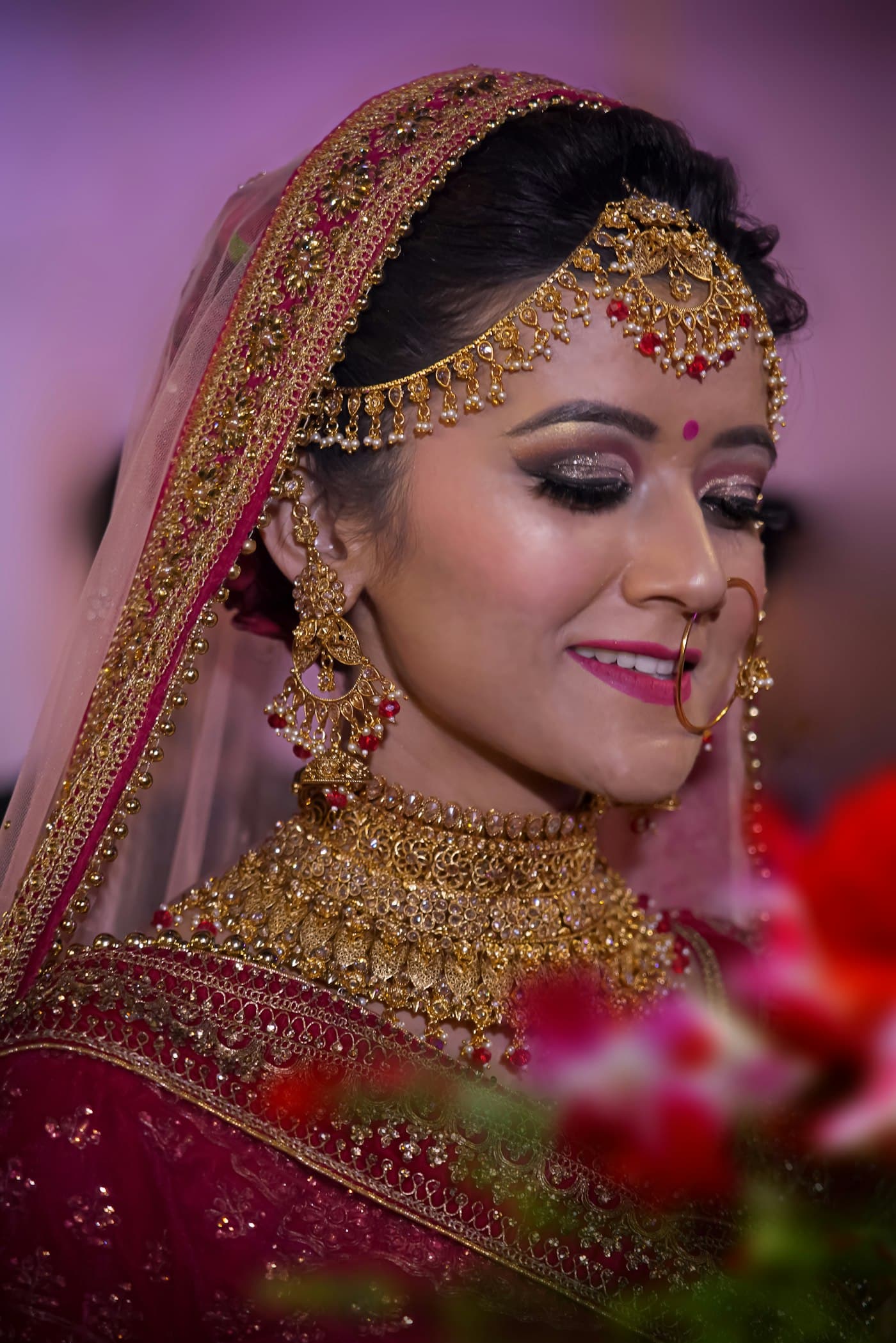 A bride wearing a gold maang tikka, nath, choker and long necklace