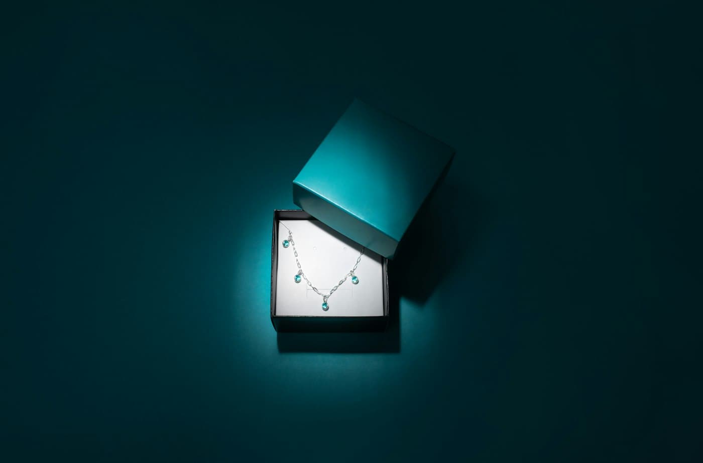 A silver necklace with blue stones lit inside an open teal jewellery box